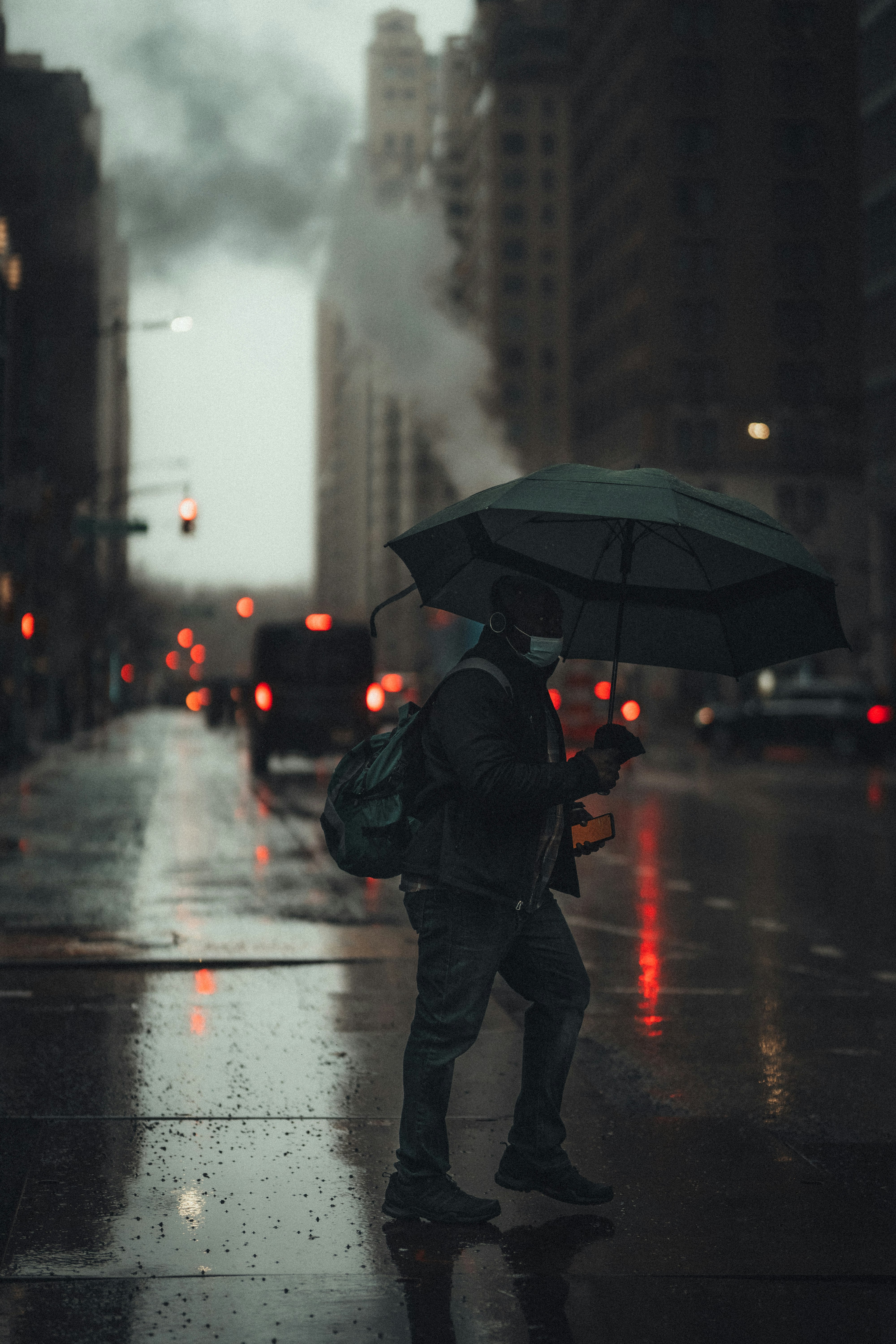 man in black jacket and pants holding umbrella walking on street during rain